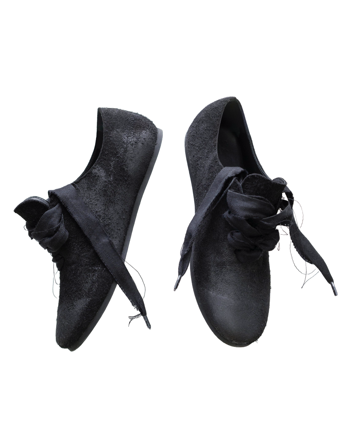A pair of black slip-on shoes with wide, knotted fabric laces and a textured, slightly distressed finish, shown against a plain white background.
