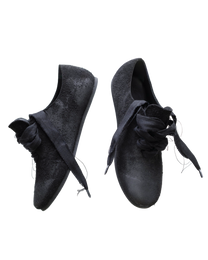 A pair of black slip-on shoes with wide, knotted fabric laces and a textured, slightly distressed finish, shown against a plain white background.